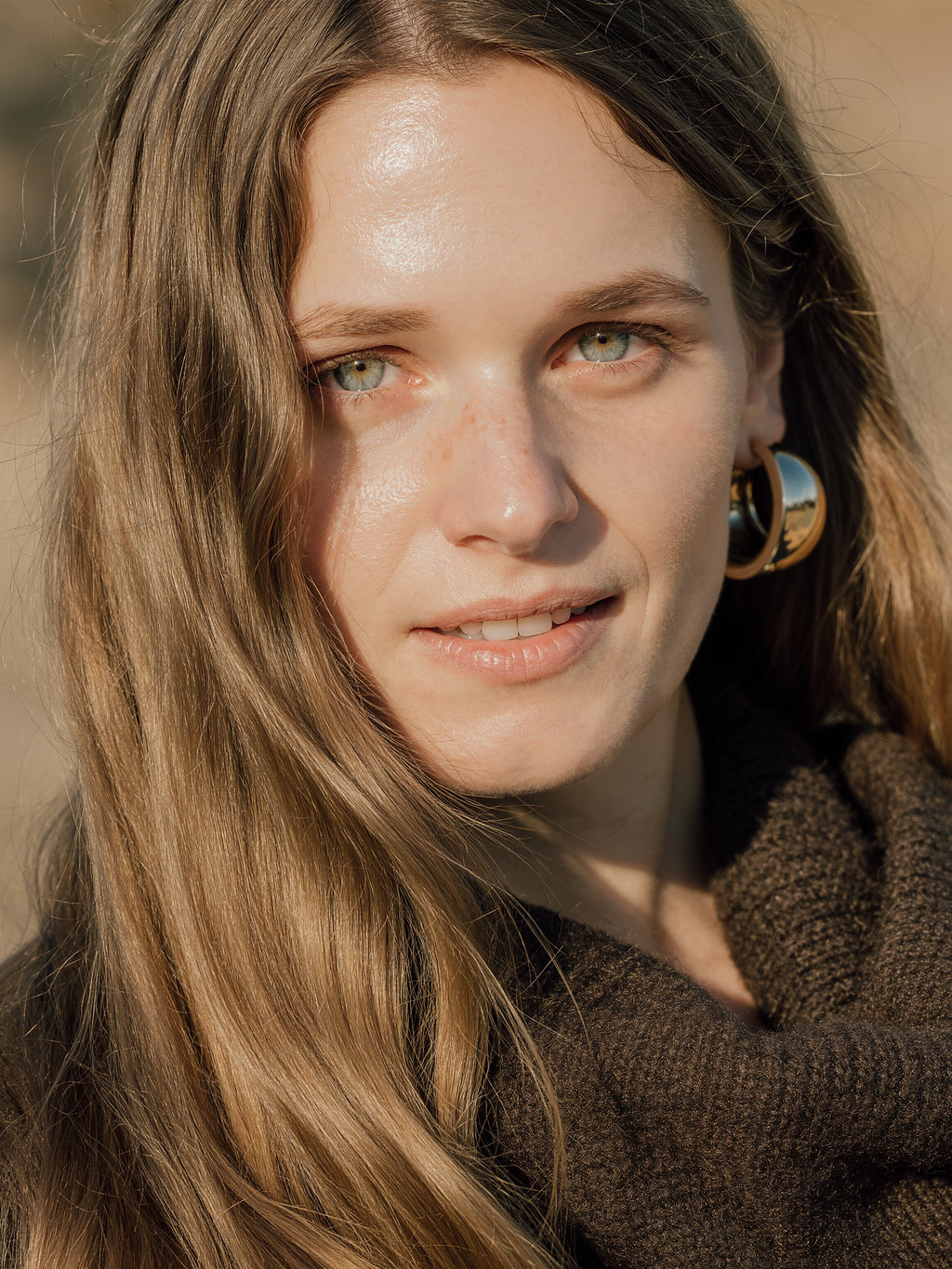Lilyanna in a cocoa knit wearing mirror-polished gold hoop earrings, glancing toward the camera.