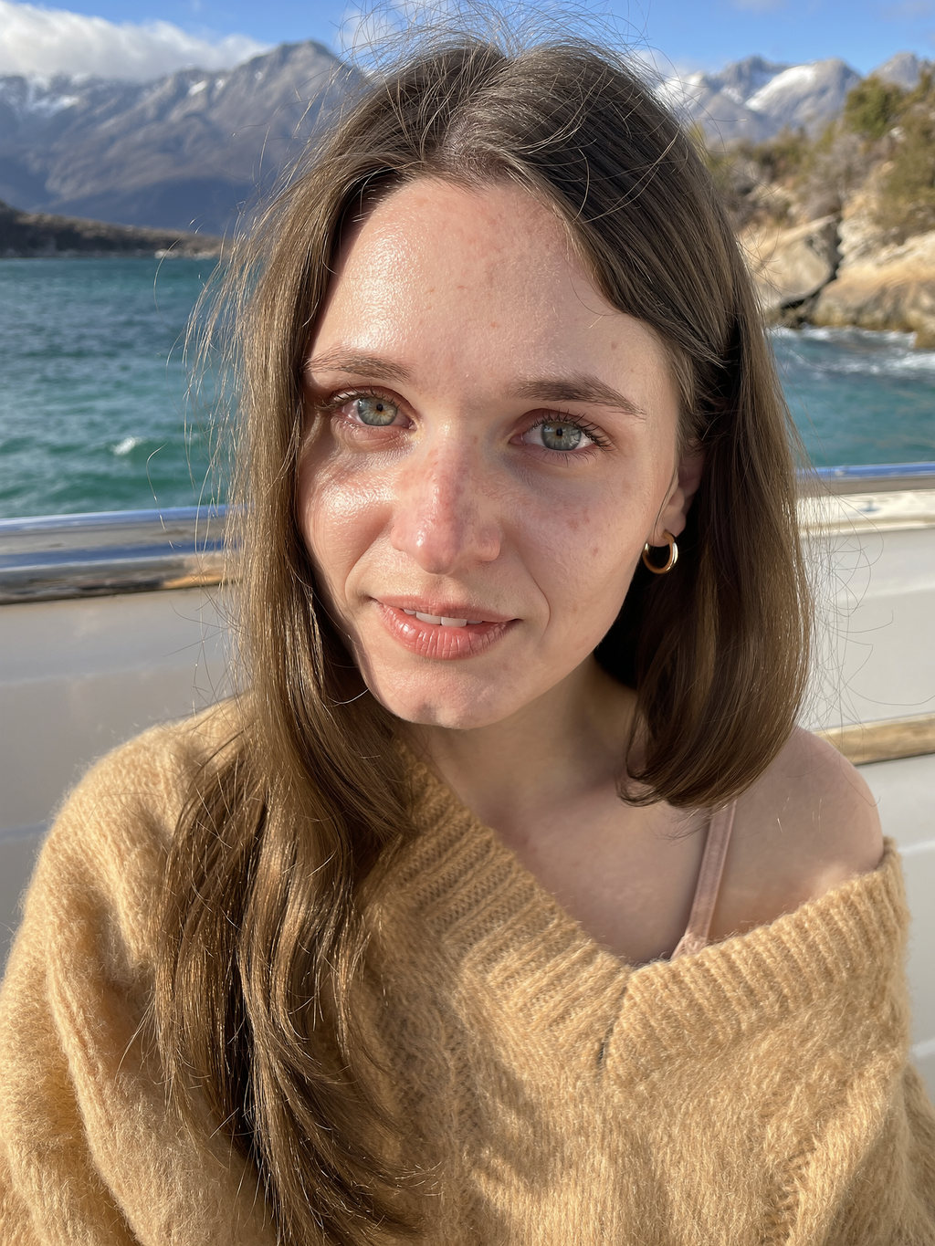 Lilyanna aboard a boat on a mountain lake in a honey mohair sweater and small gold hoops.