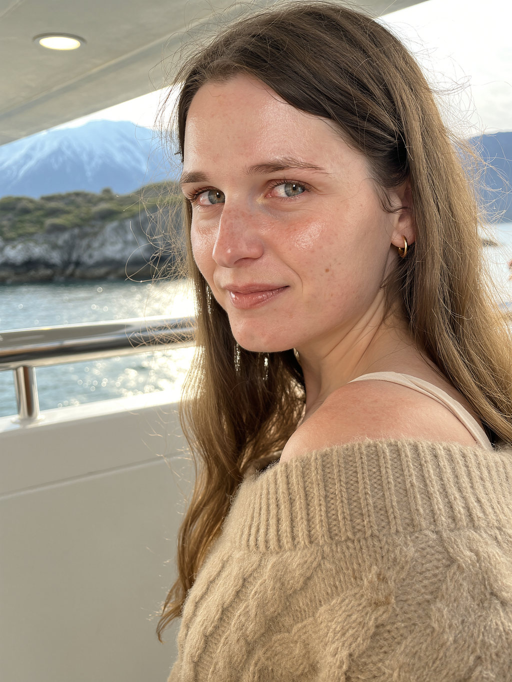Lilyanna glancing over her shoulder on a boat deck, snow-capped mountains and bright water behind her.