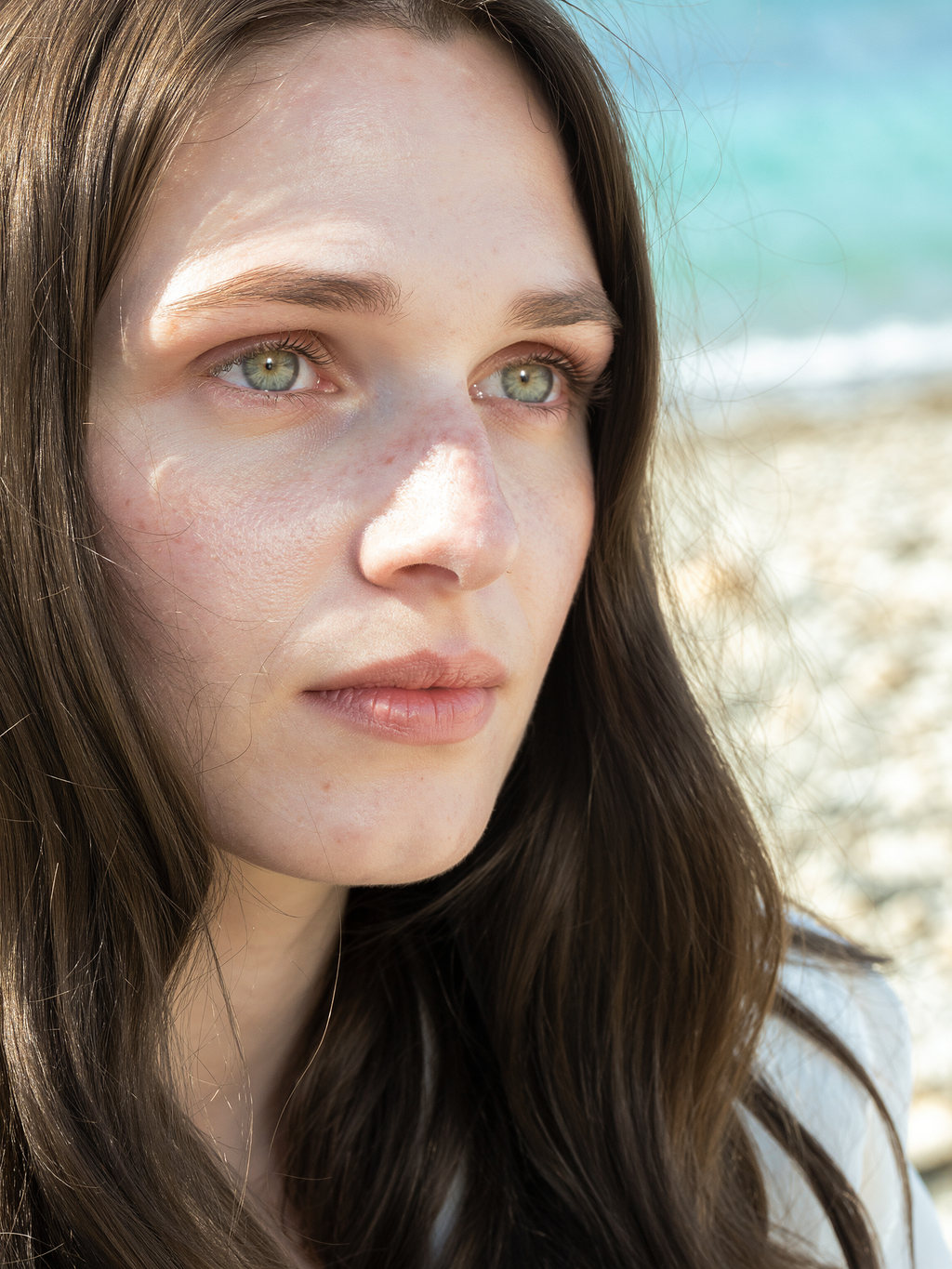 Side profile of Lilyanna by the sea, luminous skin and long dark hair in soft sunlight.
